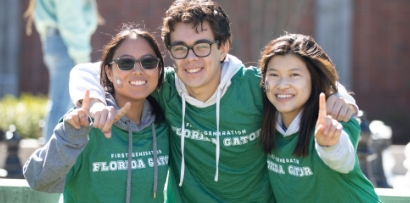 Three students in hoodies and matching green First Generation Florida Gator shirts each hold up their pointer fingers and smile