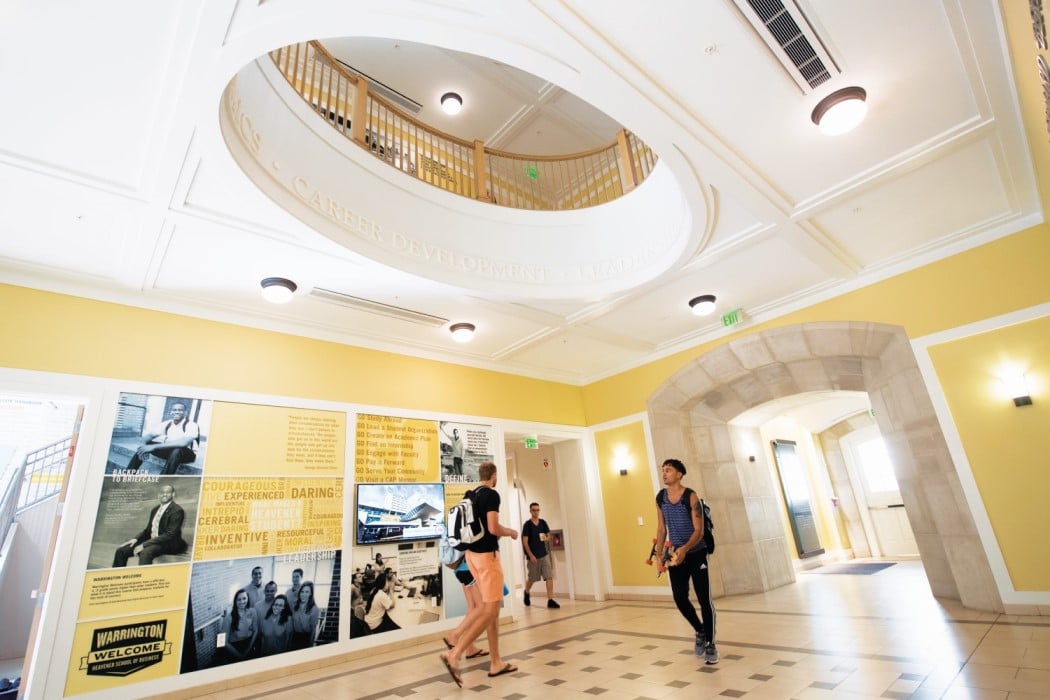 students walk along the first floor lobby of Heavener Hall underneath with the building's signature rotunda