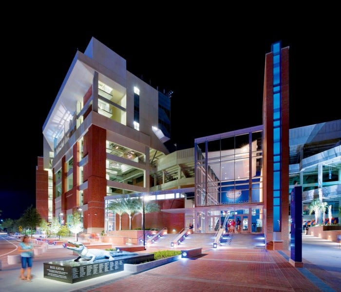 Exterior of the Steve Spurrier Stadium entrance at night, with the stadium interior lights aglow