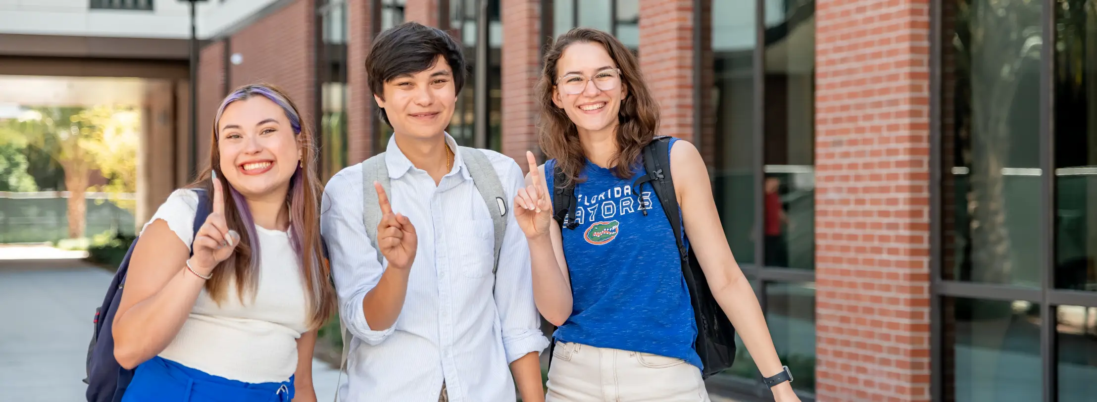 Three smiling students hold up the number one sign outside of a University of Florida building